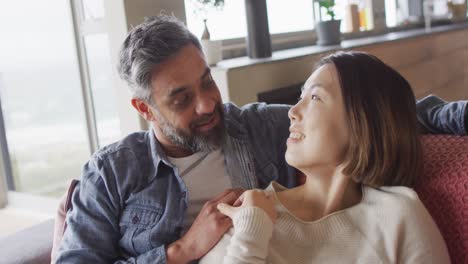 Happy-diverse-couple-sitting-in-living-room-and-talking-together