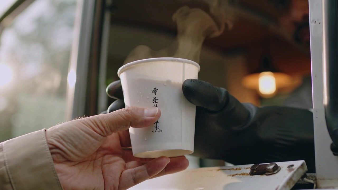 Venditore guantato che porge una tazza di carta fumante allo sportello di servizio, mentre un anziano acquista una bevanda calda.
