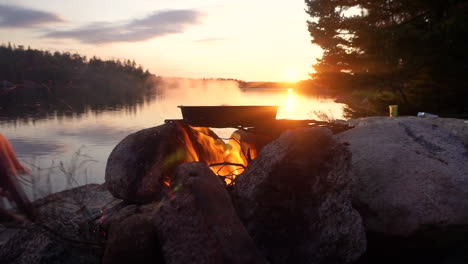 food is cooked over a campfire next to a lake during the sunset