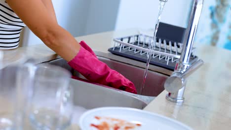a person wearing pink gloves washes dishes under running water in a modern kitchen setting