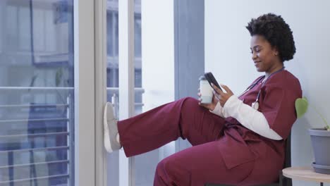 doctora afroamericana feliz usando un teléfono inteligente en el hospital, cámara lenta