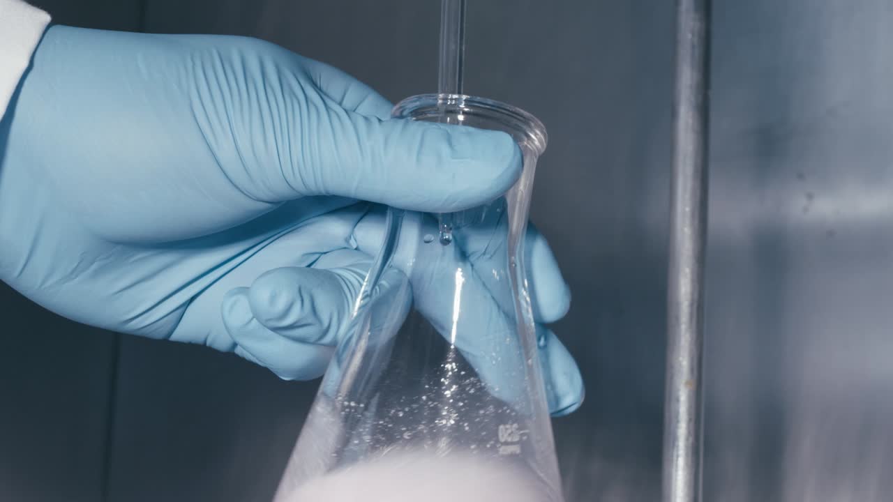 Lab worker's hand shaking serum liquid in the bottle while working in Medical Drug Production