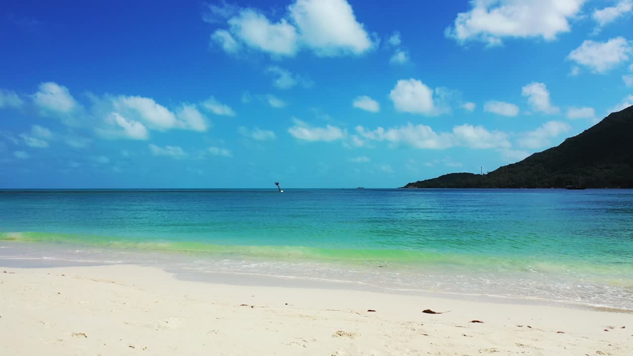 Peaceful sea scenery with white sand of exotic beach washed gently by turquoise lagoon flows under bright blue sky with white clouds
