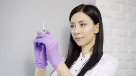 A beautiful cosmetologist with long hair checks the syringe with an injection before administering the drug to the client in the beauty salon. Aesthetic cosmetology. Close-up.