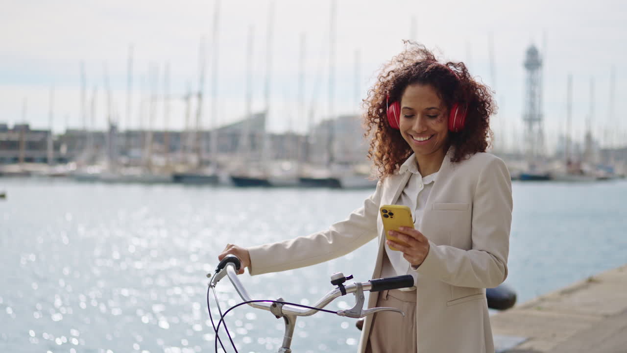 Woman with bicycle, headphones, and phone by the waterfront