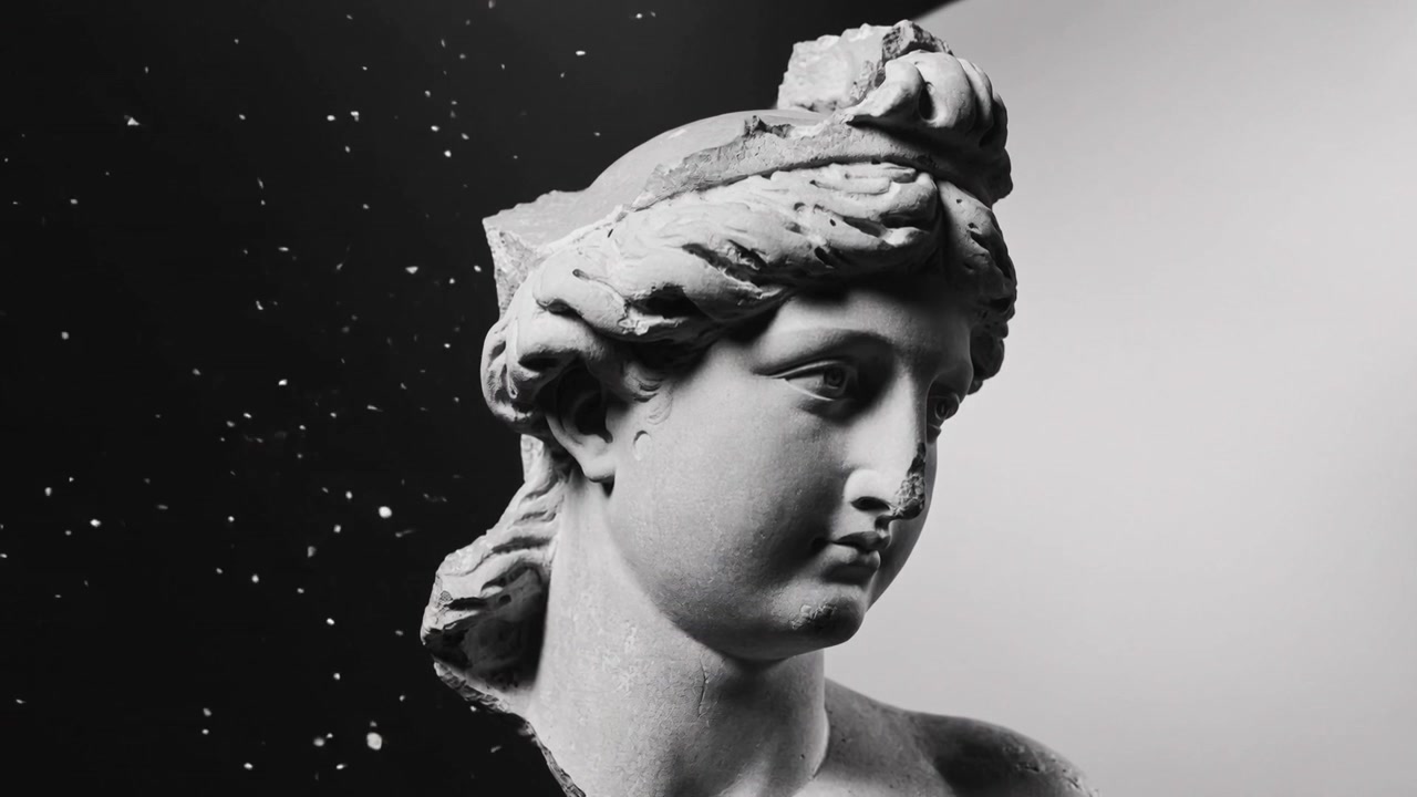 Telecamera che stringe l'inquadratura e zooma su un busto di marmo in studio, rivelando dettagli facciali e particelle fluttuanti.