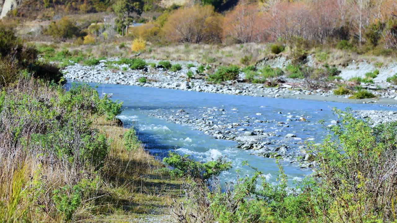 A tranquil river flows through lush greenery in Glenorchy, New Zealand, under bright natural light