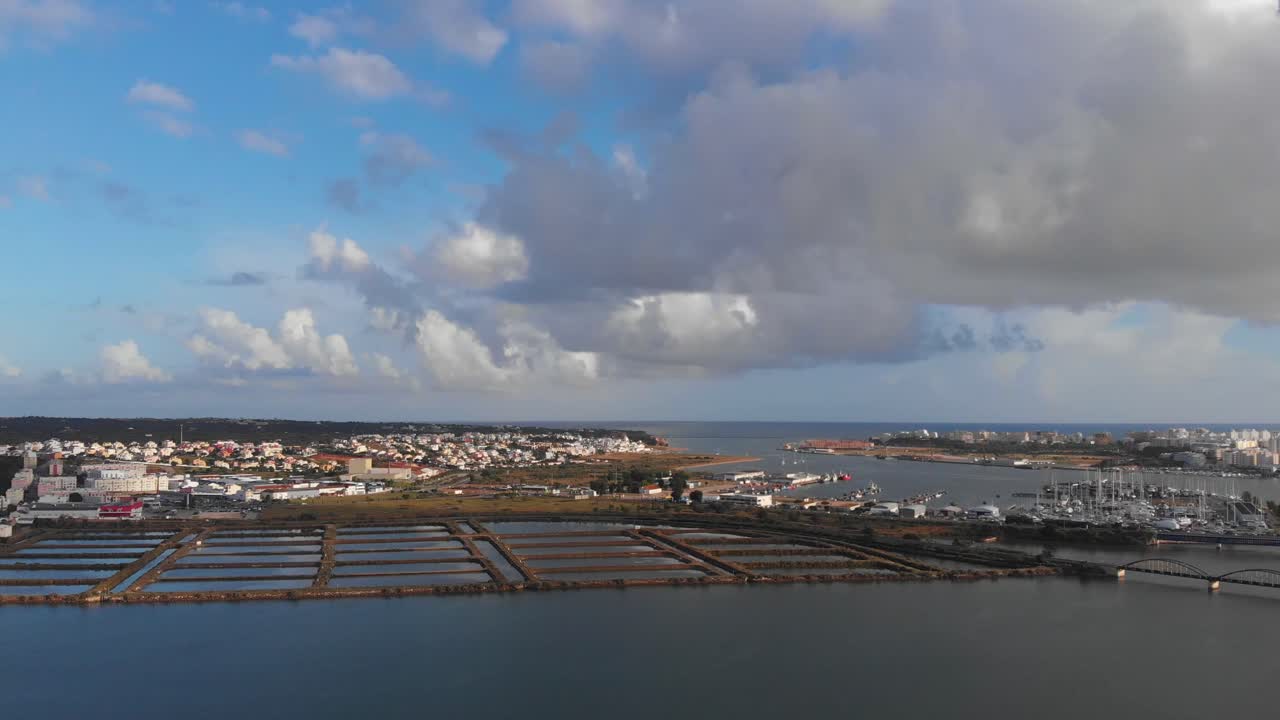 Aerial view of salt fields, old city and Arade river during sunny day with clouds in Portugal