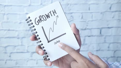 hand holding a spiral bound notebook with a growth chart drawing