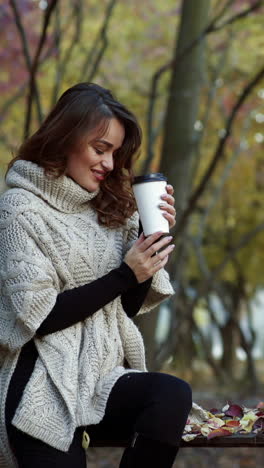 Girl drinking coffee in park. Young woman holding cup of coffee in the autumn forest Vertical video