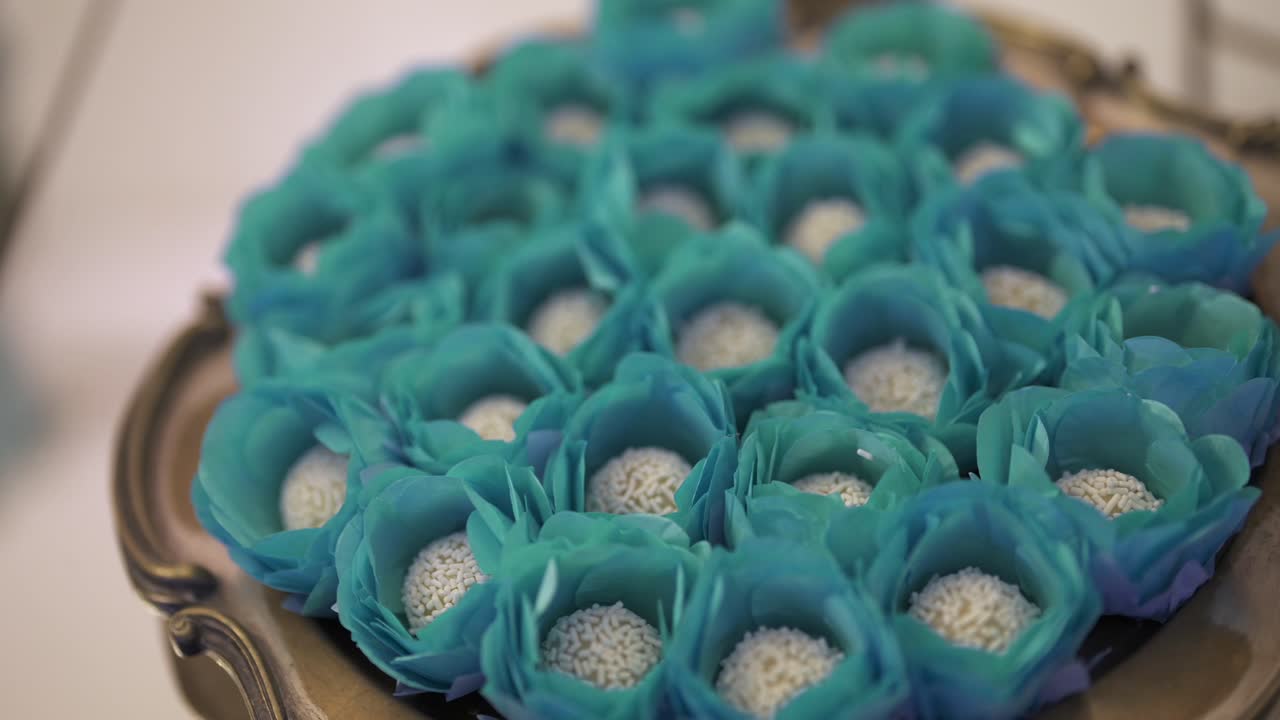 Close-up shot of cupcakes arranged on a decorative tray, with a slight camera movement revealing blue flower-style wrappers