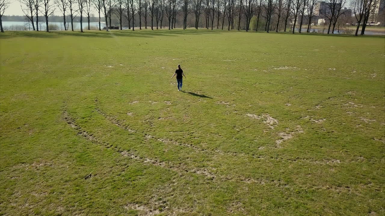 공원에서 검은색 티셔츠를 입은 성인 여성을 따라 앞으로 날아가는 공중 드론 샷