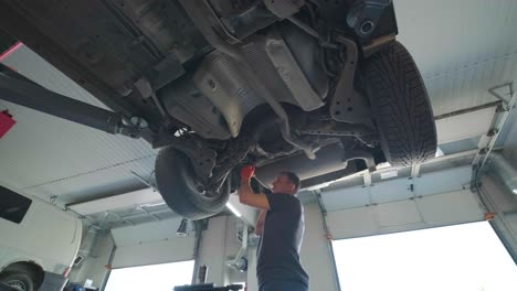 young professional mechanic man working under lifted modern car in auto repair service. car service, repair maintenance.