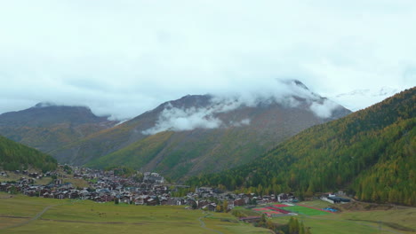 Swiss-Alps-Saas-Fee-Saastal-Switzerland-aerial-drone-flight-over-mountain-alpine-valley-glacier-town-chalets-gondola-rainy-foggy-mist-grey-clouds-wet-fall-autumn-forward-up-motion