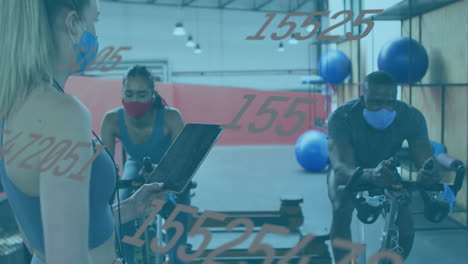 animation of numbers changing over female instructor, woman and man in face masks on bikes in gym