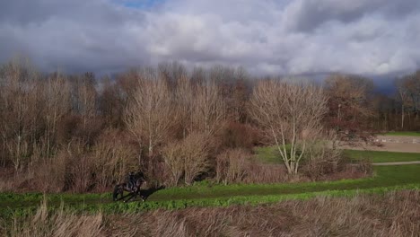 Horseback-Riding-On-The-Green-Field-Surrounded-By-Bare-Trees