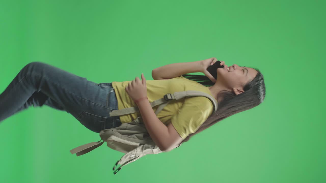 vista lateral de una estudiante asiática hablando por teléfono móvil y corriendo a la escuela en pantalla verde clave de croma
