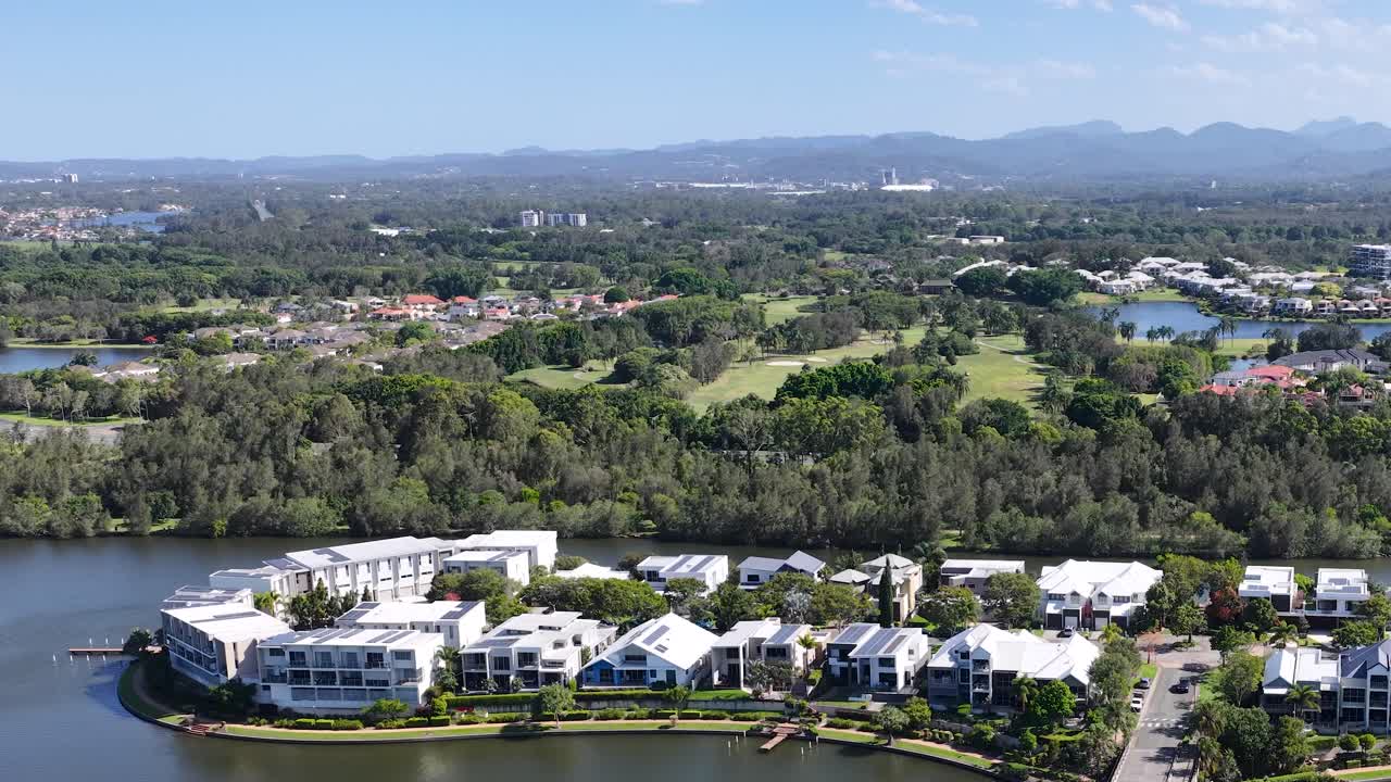 Drone slowly pans above lakeside residential neighborhood, golf course, and distant skyline in sunlight