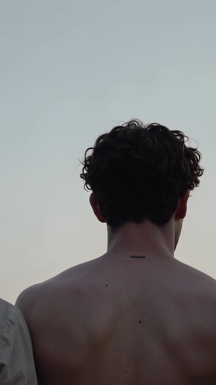 Vertical video: Tightening camera causing shirtless man turning head at dawn, revealing neck tattoo