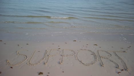 static shot of support written in the sand on a beach with water lapping onto the sand