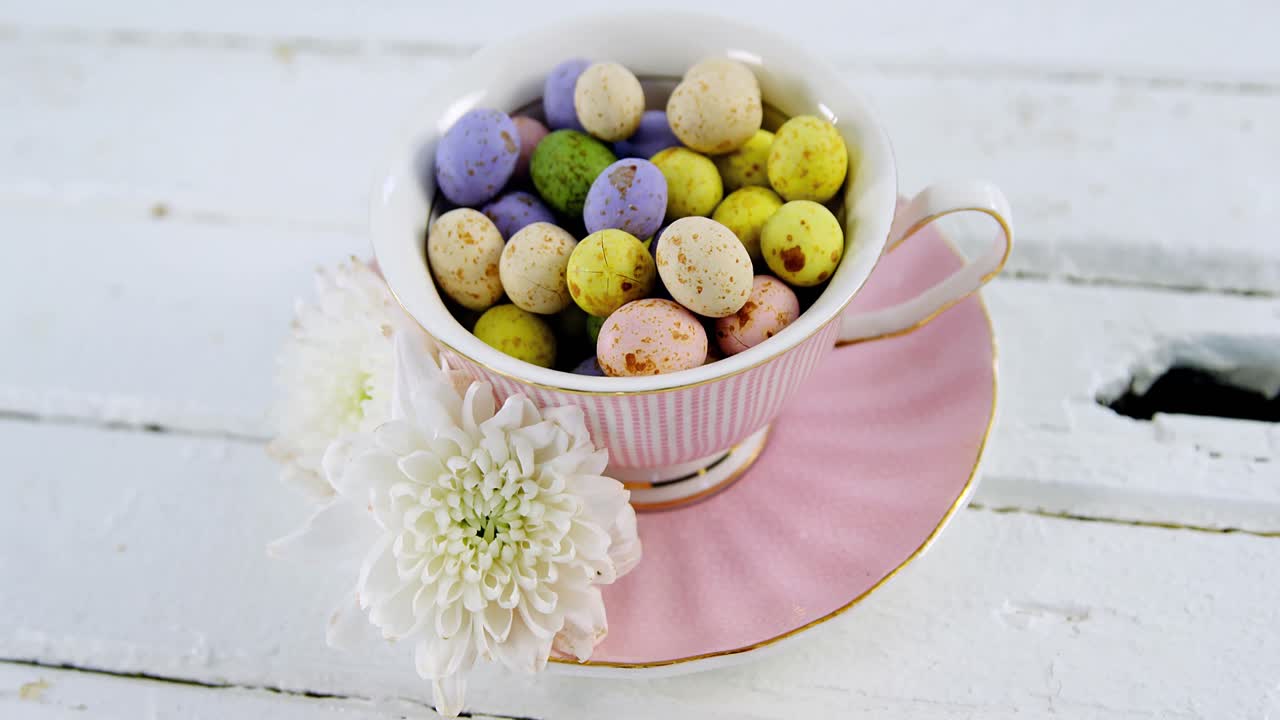 Cup filled with painted chocolate Easter eggs and white flower