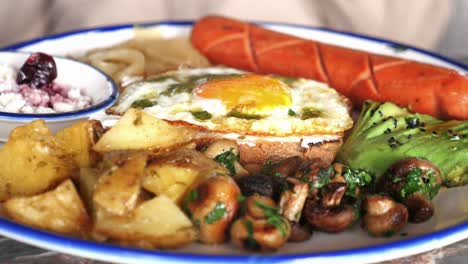 abundante plato de desayuno con huevo frito, salchichas, aguacate y patatas asadas
