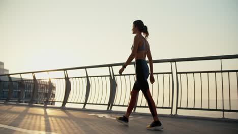 a young athletic girl in sportswear walks along the bridge in the city in the morning. sunrise and morning run