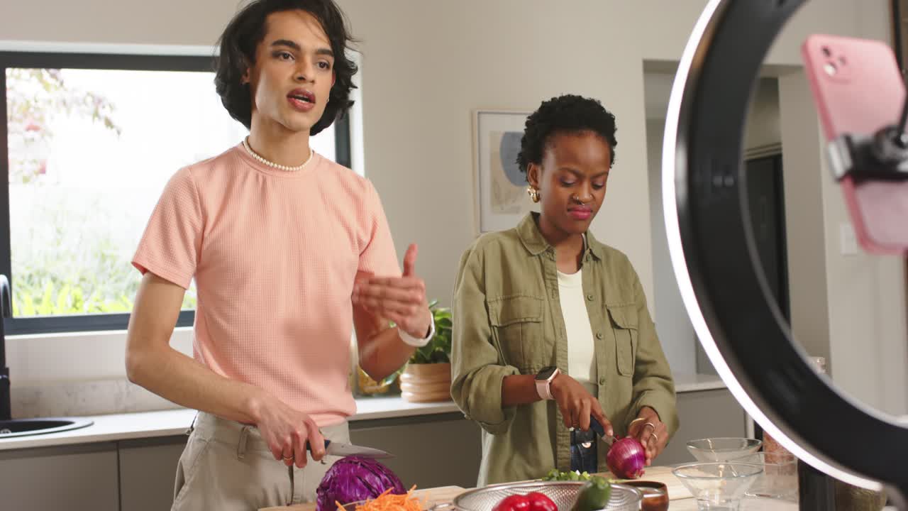 Diverse co-hosts entering home kitchen and chopping veggies by ring light for cooking tutorial