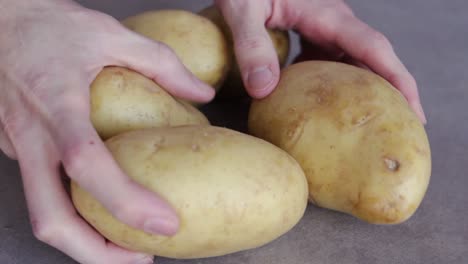 person's hand put five raw potatoes on the table