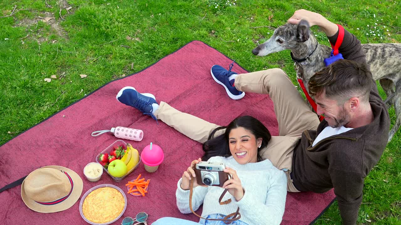 Glückliches Paar und Windhund genießen ein Picknick im Park.