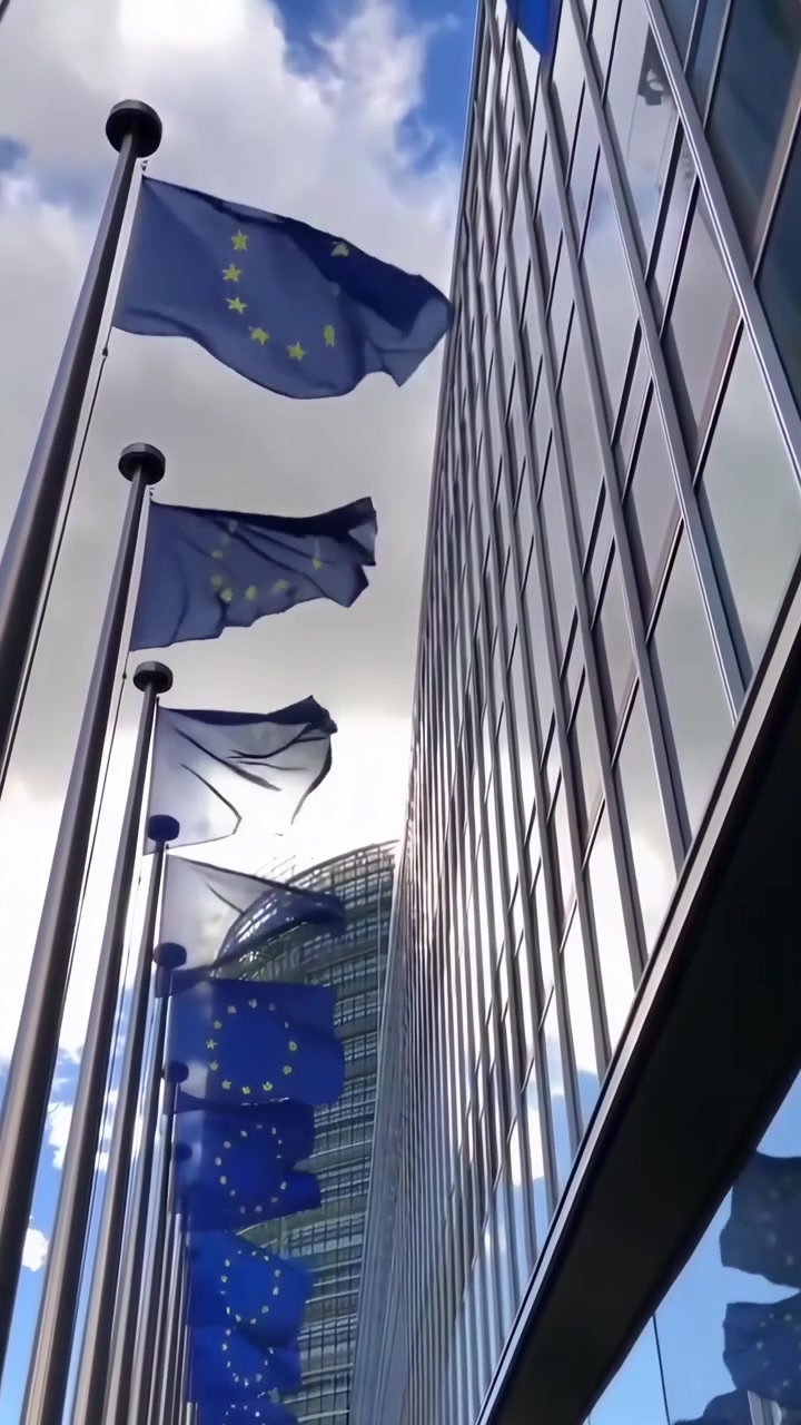 Bandiere dell'UE che sventolano davanti a un moderno edificio in vetro e un cielo nuvoloso