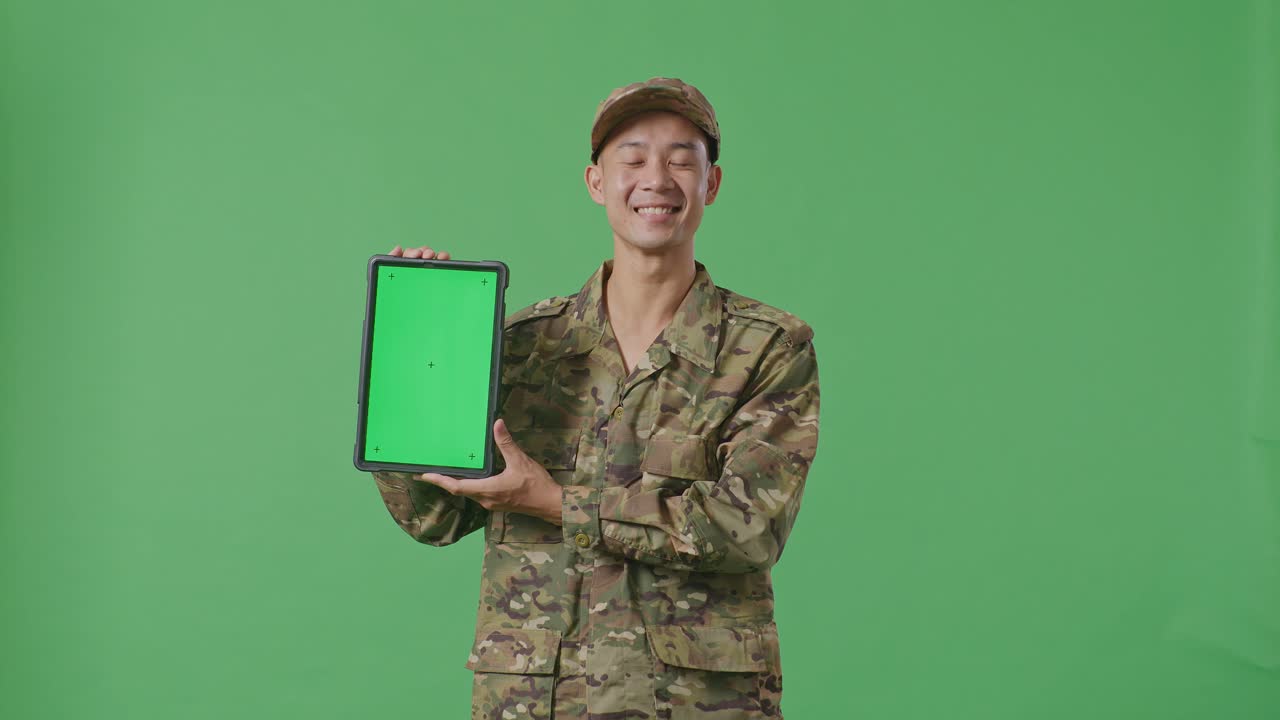 Asian Man Soldier Smiling And Showing Green Screen Tablet To The Camera While Standing In The Green Screen Background Studio