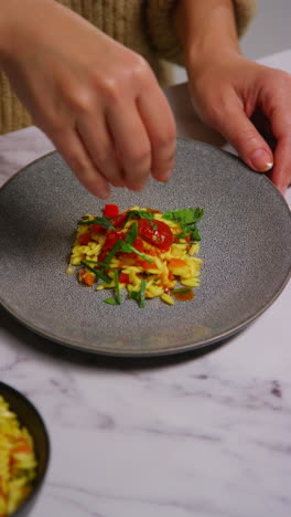 vertical video close up of woman at home in kitchen preparing healthy vegetarian or vegan meal sprinkling herbs onto orzo pasta and roasted tomatoes 1