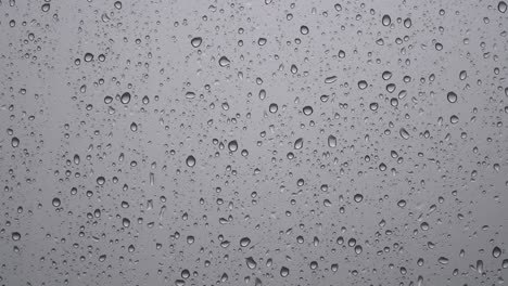 raindrops on blurry grey glass window - rainy day elements - close up