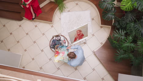 man creates portrait of lady in red in home studio. skilled portraitist combines colors on palette against lady sitting in gallery. artwork creating process