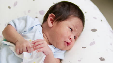 stretching its arms and looking up to the right side of the frame, a baby is lying on a mattress inside a crib