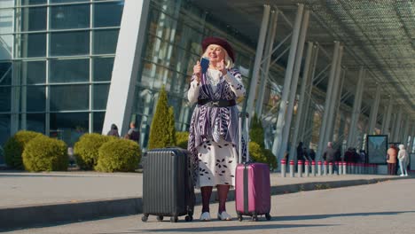 Elderly-retired-woman-tourist-near-airport-terminal-celebrating-success,-winning-and-goal-achievemen