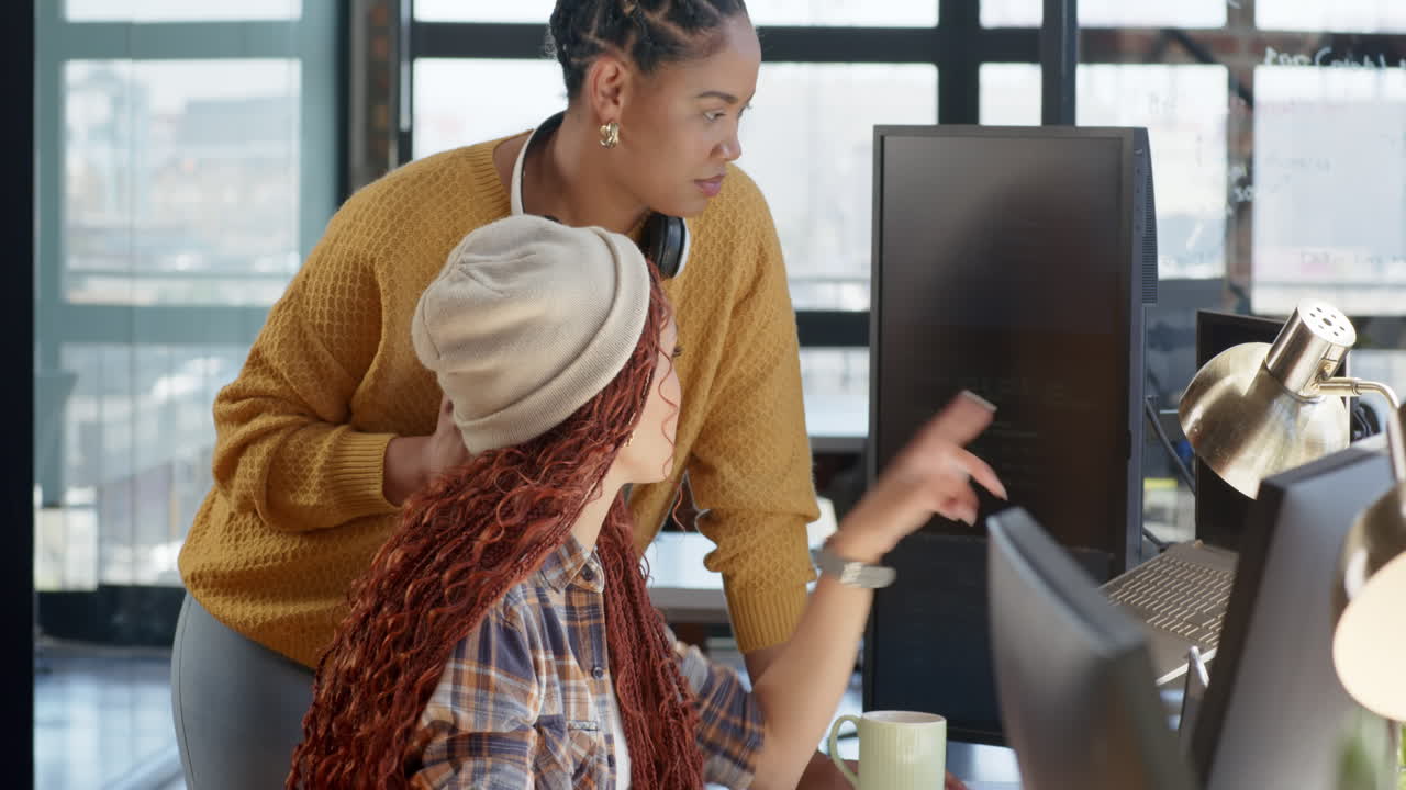 Collaborating on coding project, diverse female team using computer and smartphone in office
