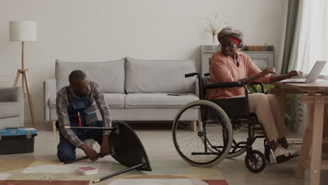 Handicapped Woman Working on Laptop while Handyman Assembling Furniture
