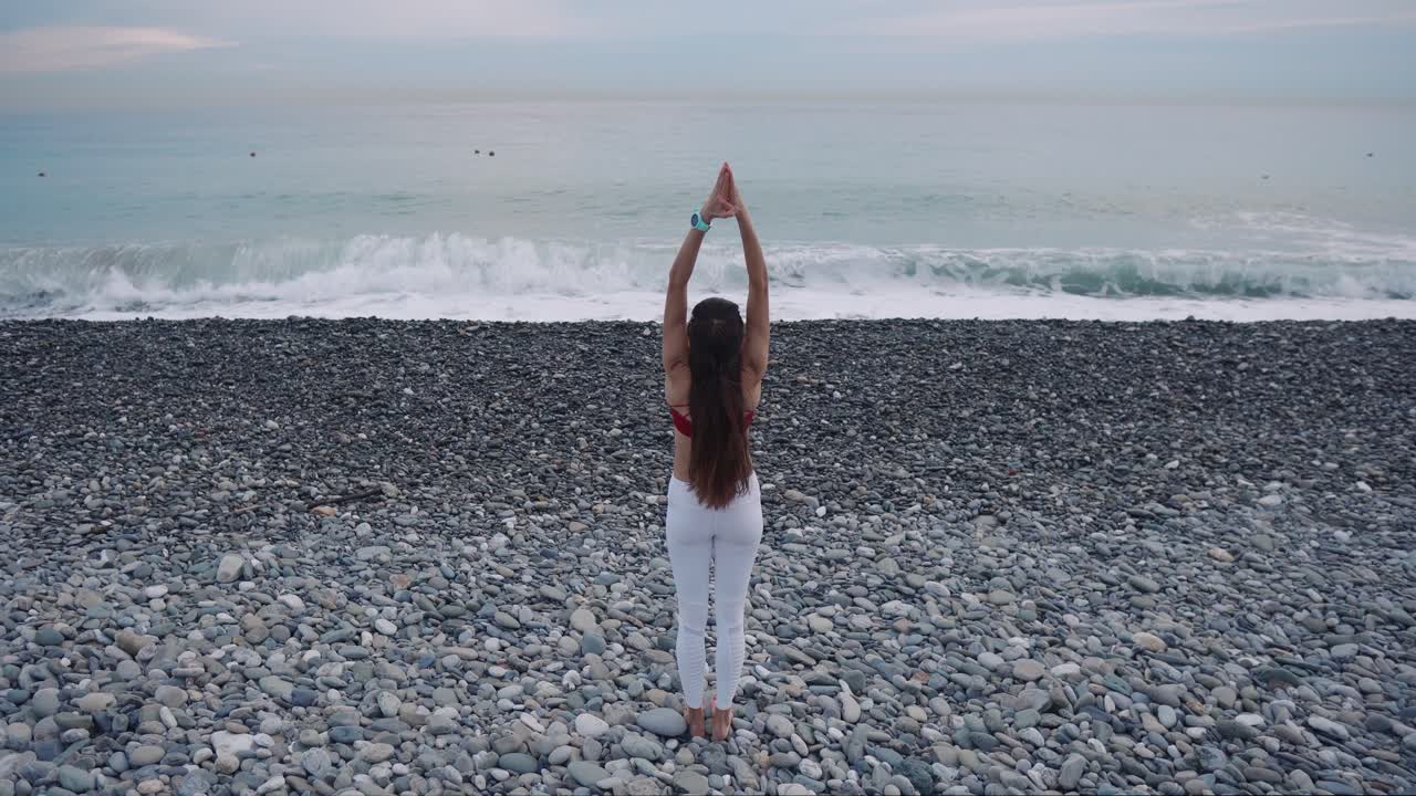 mujer practicando yoga en una playa de guijarros