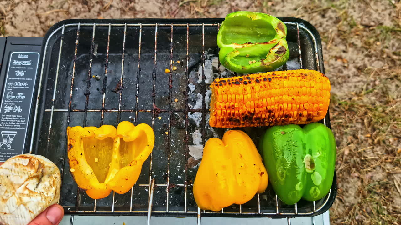 Grilling fresh corn and bell peppers on metal barbecue grill in outdoor setting