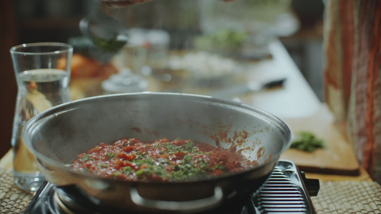 primer plano de la adición de hierbas frescas a la salsa de tomate hirviendo en la sartén