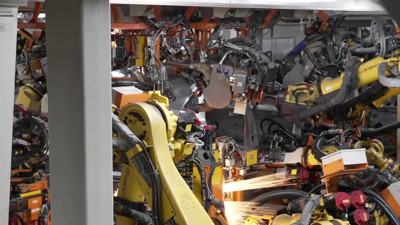 Close up of multiple robotic welding arms working simultaneously on a car frame with bright sparks in a dense industrial setting