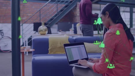 animación de dos globos de iconos digitales girando sobre una mujer biracial usando una computadora portátil en la oficina
