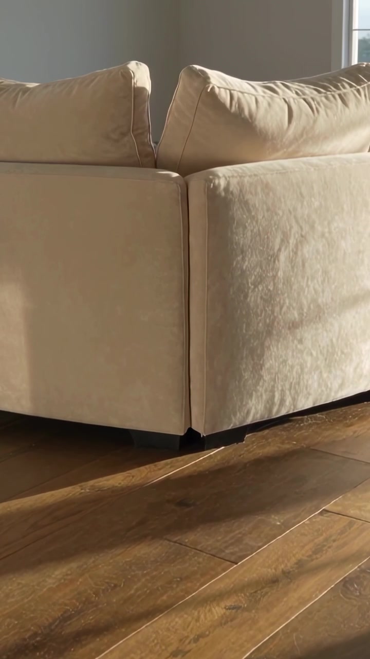 Video vertical: Cámara inclinándose revelando la esquina de un sofá beige en casa, mostrando una franja de suelo de madera iluminada por el sol.