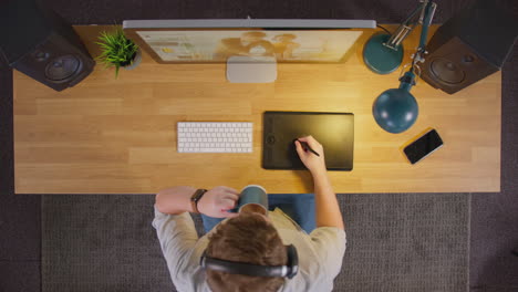 Overhead-View-Of-Male-Graphic-Designer-Working-At-Computer-Screen-In-Creative-Office-At-Night