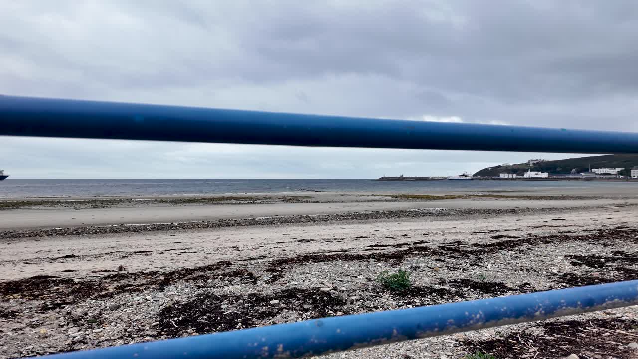 Blue railing framing the Douglas beach shoreline with sea and harbor in the background