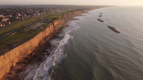 panorama aerial shot of lighting rocky cliffs and crashing waves from atlantic ocean during sunset - golden sunset time at horizon in suburb area of south america