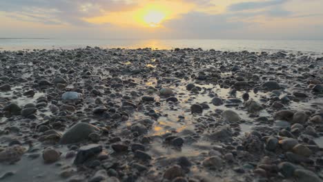 Glistening-pebbles-on-shoreline-with-approach-to-very-calm-sea-during-sunset-in-slow-motion-at-Fleetwood,-Lancashire,-UK