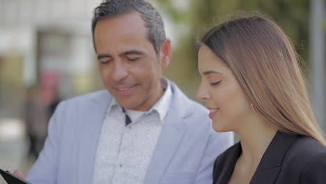 hombre y mujer sonrientes usando una tableta en la calle